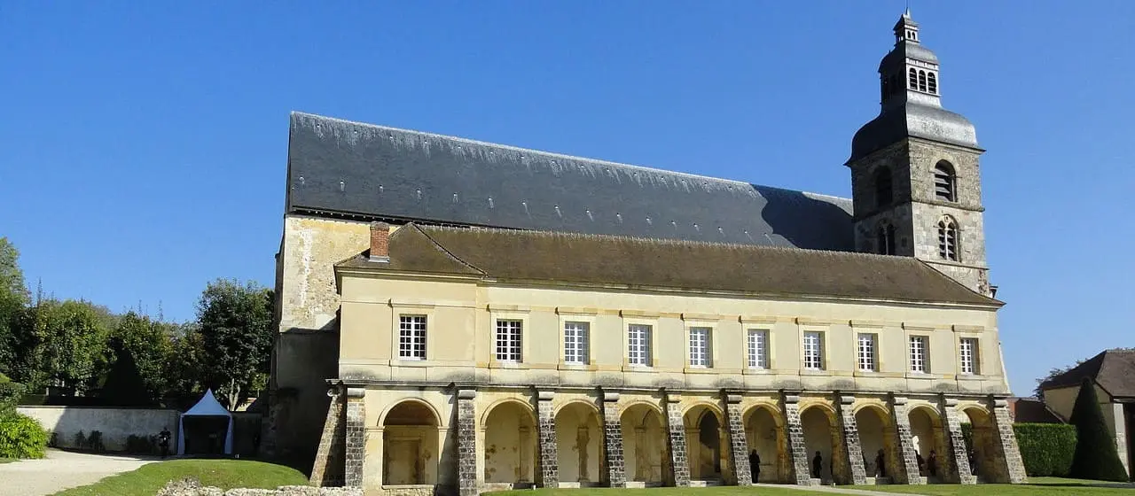 A side view of the Abbey Saint Pierre in Hautvillers, featuring a long building with arched windows and a tall bell tower against a clear blue sky