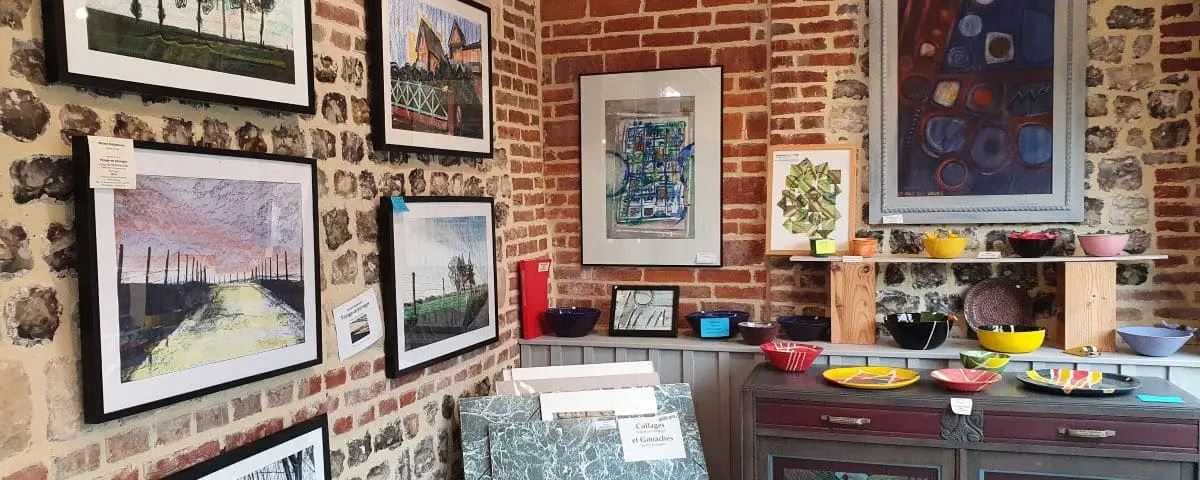 A cozy art gallery with brick walls displaying various framed paintings. The scene includes pottery on shelves and a table in the foreground.