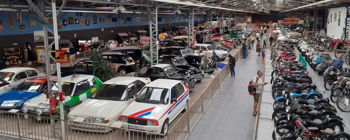 A wide panorama of the bustling Automobile Museum in Reims, showcasing a diverse collection of vintage cars and motorcycles, a perfect cultural attraction on a Paris to Reims day trip.