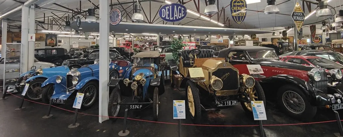 An exhibit at the Automobile Museum in Valençay showcasing a collection of vintage cars, including blue and black models, under a large indoor display with signage for different car brands.