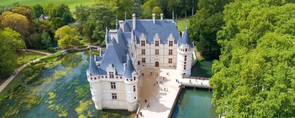 Aerial view of the Azay-le-Rideau Castle surrounded by lush greenery and a moat, with visitors exploring the castle grounds.