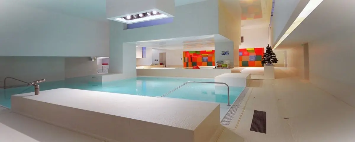 The modern indoor pool area at Bains des Docks in Le Havre, with geometric architecture, white walls, and colorful accents.