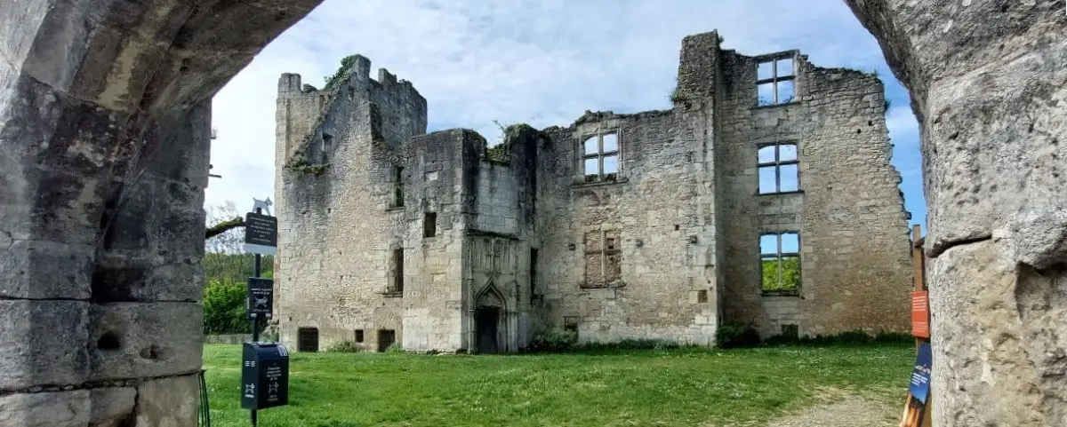 The ruins of Barrière Castle in Périgueux, displaying weathered stone walls and window openings without glass. The scene is framed by a stone archway, highlighting the castle's historical and architectural significance.