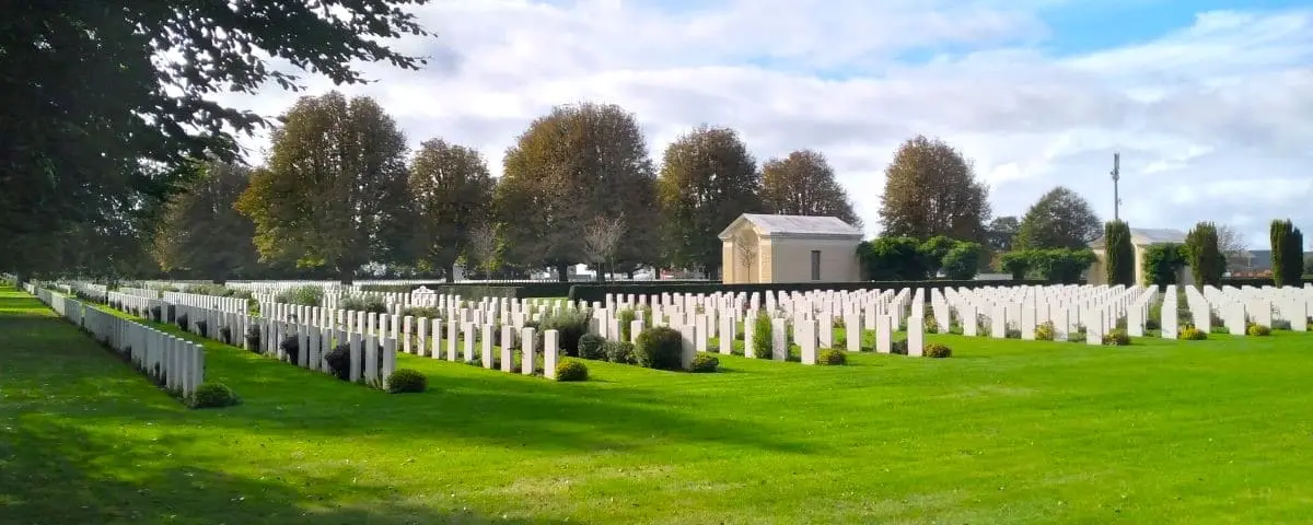Rows of white headstones in a well-maintained cemetery, with green grass and trees in the background, honoring British soldiers.