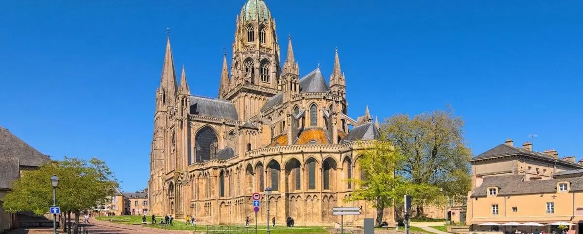 The impressive Gothic architecture of Bayeux Cathedral, with its towering spires and detailed stonework, set against a clear blue sky.