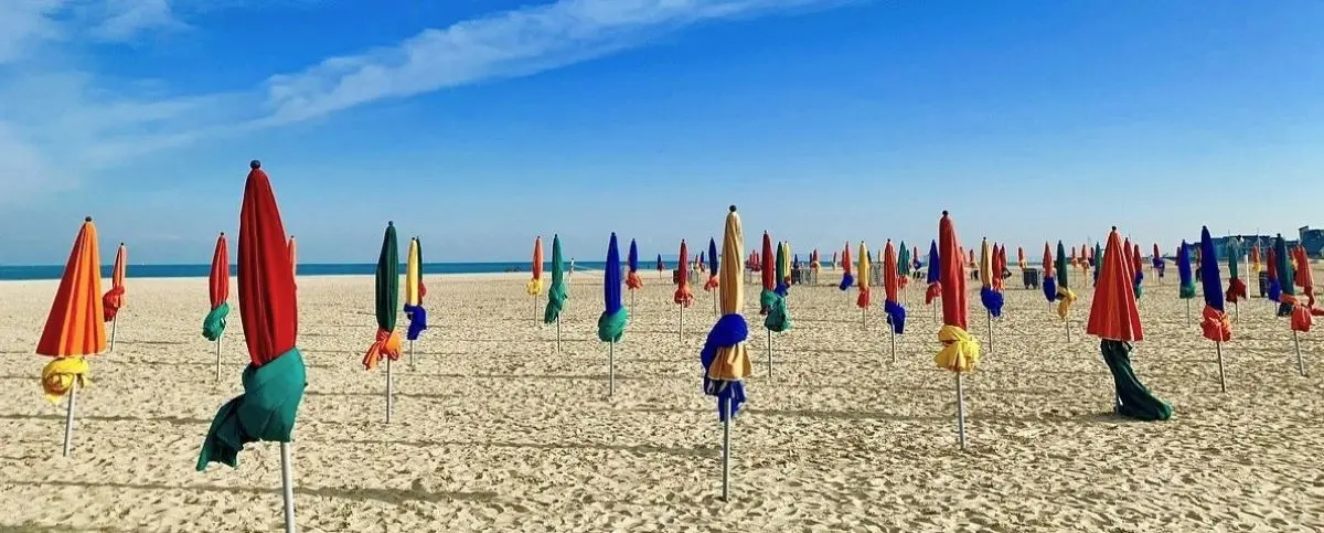 Colorful umbrellas stand closed on the sandy beach of Deauville under a clear blue sky.
