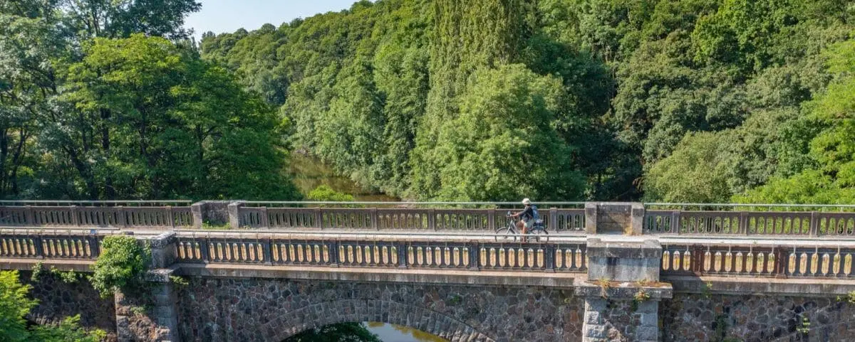 A cyclist riding on a bridge surrounded by lush green forest in Normandy, capturing the essence of a peaceful countryside bike ride.