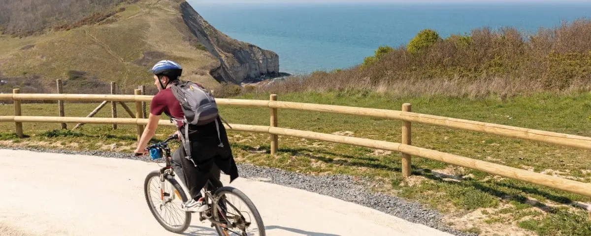 Cyclist riding along a coastal path with a view of cliffs and the ocean in Normandy, epitomizing a scenic coastal biking experience.