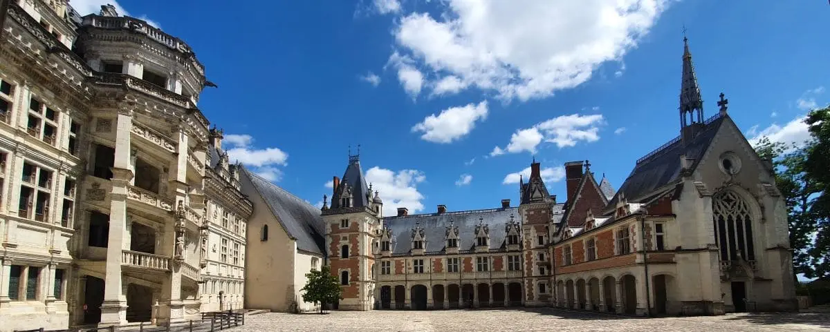 A grand historic castle with intricate architectural details, including a mix of Gothic and Renaissance styles, under a bright blue sky.