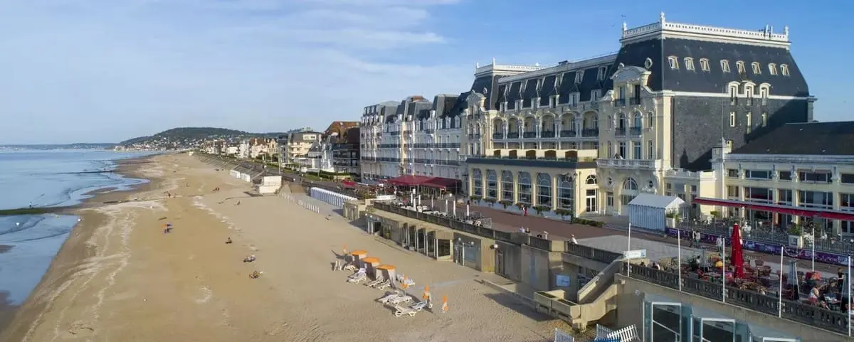 View of Cabourg's beachfront lined with grand, historic buildings, sunbathers on the sandy beach, and a clear, calm sea.