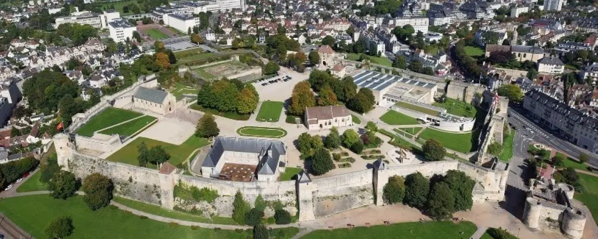 Aerial view of the historic Caen Castle, showcasing its fortified walls and well-maintained grounds. The surrounding cityscape highlights the castle's prominence in the area.