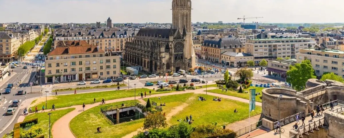 A panoramic view of Caen city highlighting the central St. Peter's Church and the surrounding urban landscape with green spaces and roads.