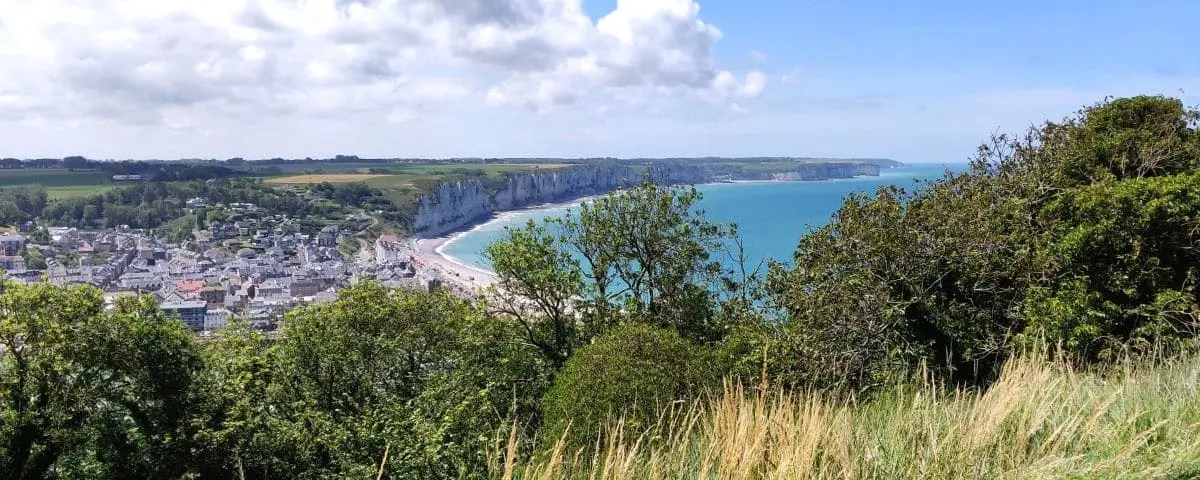 A panoramic view of Fécamp from Cap Fagnet, showing the coastal town, lush greenery, and dramatic white cliffs along the coastline.