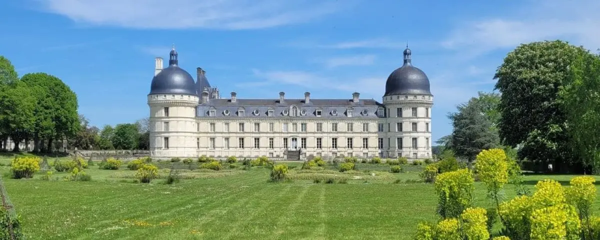 The grand Castle of Valençay, featuring a symmetrical design with two large domed towers, expansive lawns, and surrounding gardens under a clear blue sky.