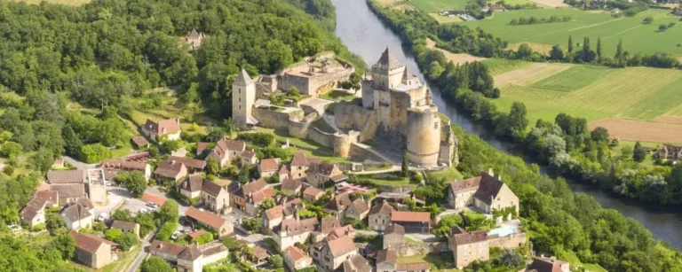 An aerial view of Castlenaud-la-Chapelle village in Dordogne, featuring a medieval castle surrounded by charming houses and a river winding through the lush landscape.