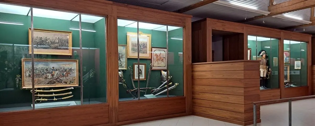 Exhibit in the Cavalry Museum in Saumur, featuring glass cases with historic paintings, swords, and military uniforms.
