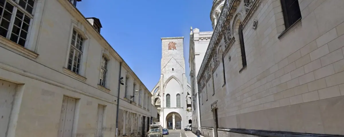 A tall, historic clock tower in Tours, France, surrounded by other buildings under a blue sky, featuring detailed stonework and clock faces on each side.