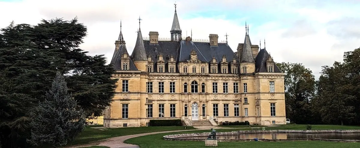 he grand Château Boursault with its intricate architectural details and pointed towers, set against a backdrop of trees and a cloudy sky.