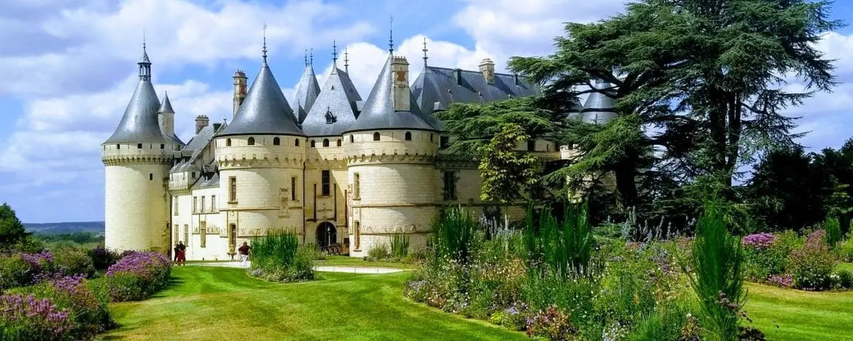 Majestic view of Chaumont-sur-Loire Castle with its conical towers, stone walls, and lush gardens filled with blooming flowers and greenery.