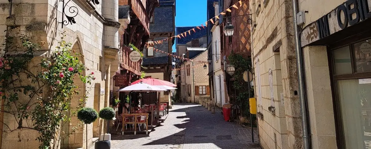 A picturesque street in Chinon's town center lined with old stone buildings, quaint shops, and a café with outdoor seating under a red umbrella.