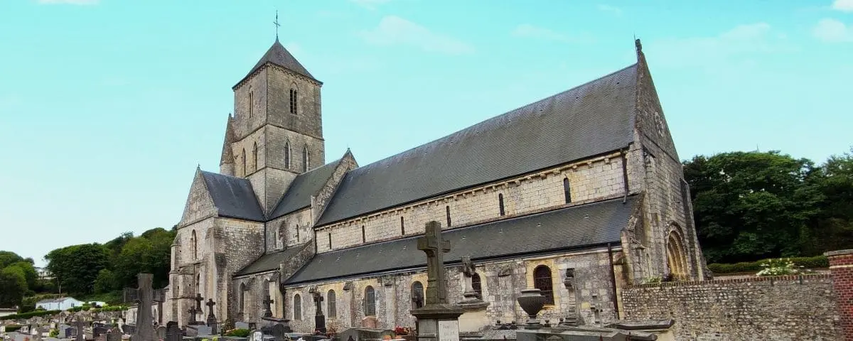 The historic Church of Notre Dame in Etretat, showcasing its stone facade and towering steeple, with a peaceful graveyard in the foreground.