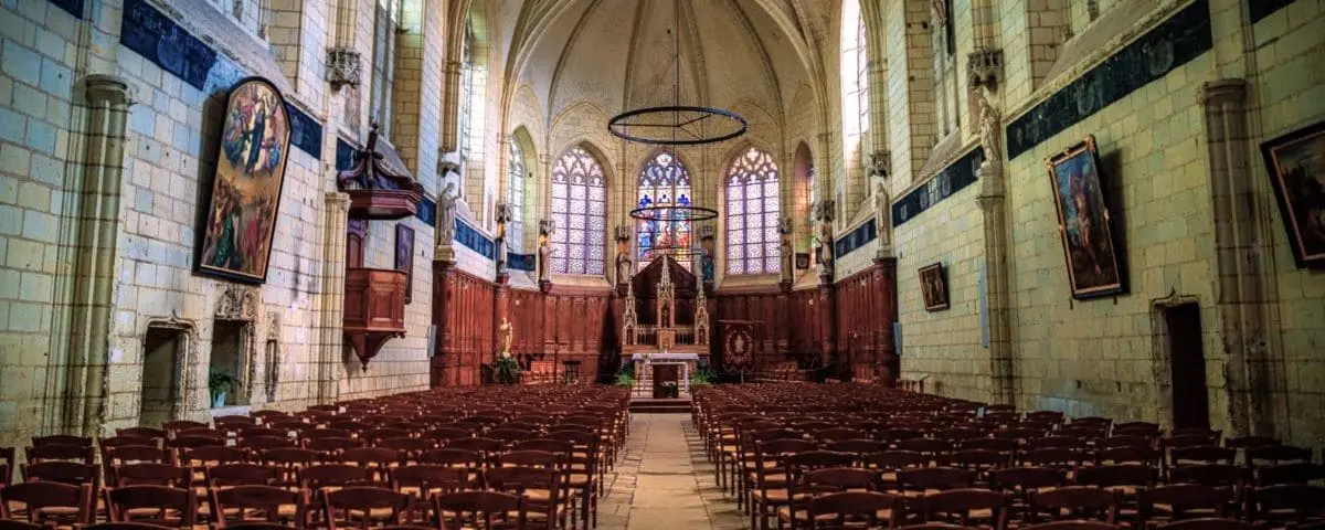 The interior of the Church of Notre-Dame in Montreuil-Bellay, featuring a grand altar, wooden pews, and high arched ceilings with stained glass windows.