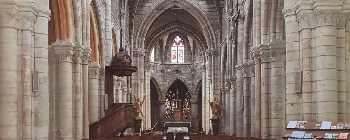 The interior of a gothic church with high vaulted ceilings, stone columns, and a detailed altar. Stained glass windows allow colorful light into the space.