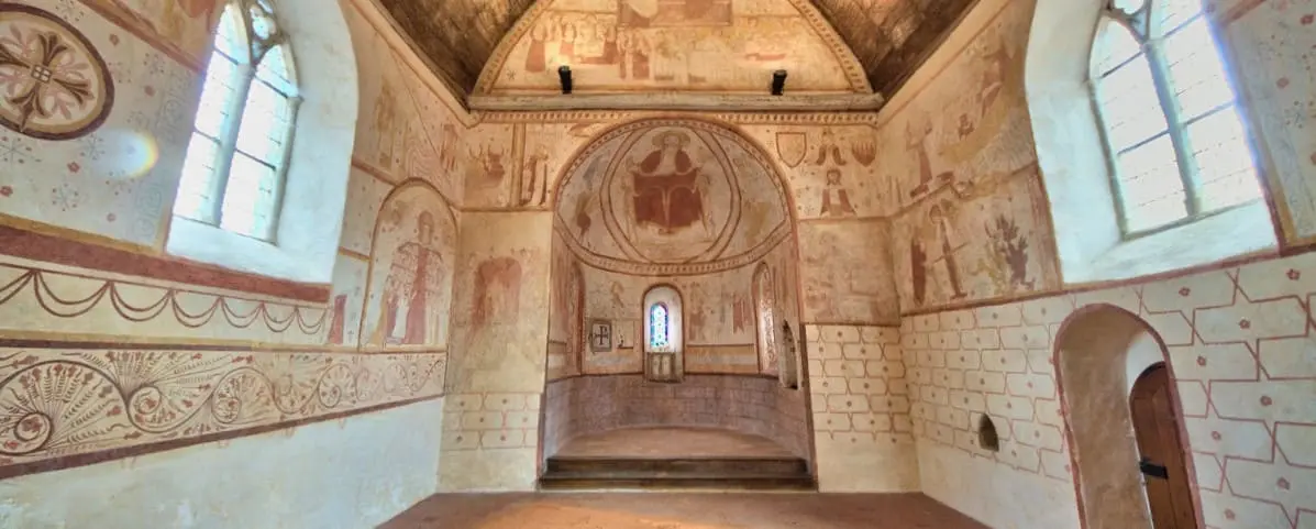 The interior of an old church featuring well-preserved frescoes and murals with religious themes. The arched windows allow natural light to illuminate the detailed artwork on the walls.