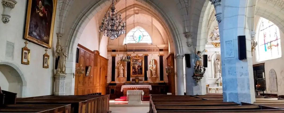 The interior of the Church of Saint-Etienne in Cheverny, showcasing a beautiful altar, wooden pews, chandeliers, and stained glass windows.