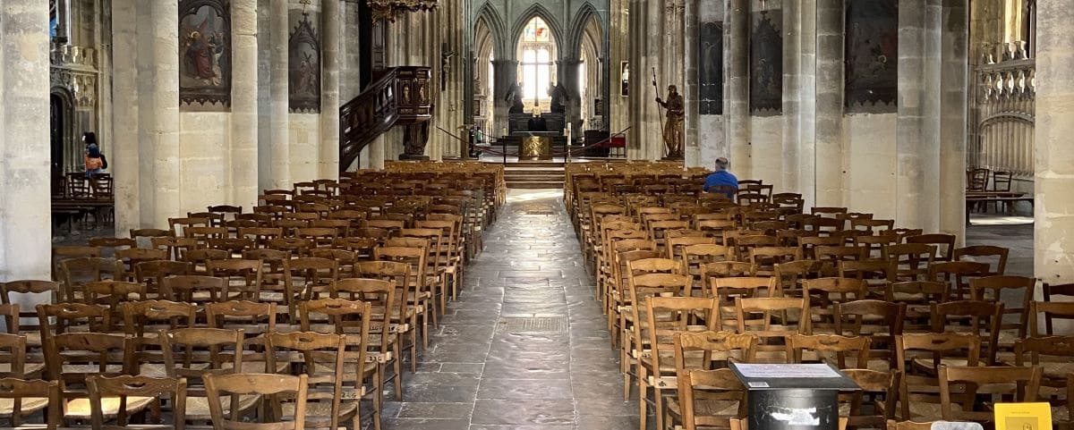 The interior of the Church of Saint-Jacques in Dieppe, showcasing rows of wooden chairs and the central aisle leading to an ornate altar. The gothic architecture is highlighted by the tall columns and arches.