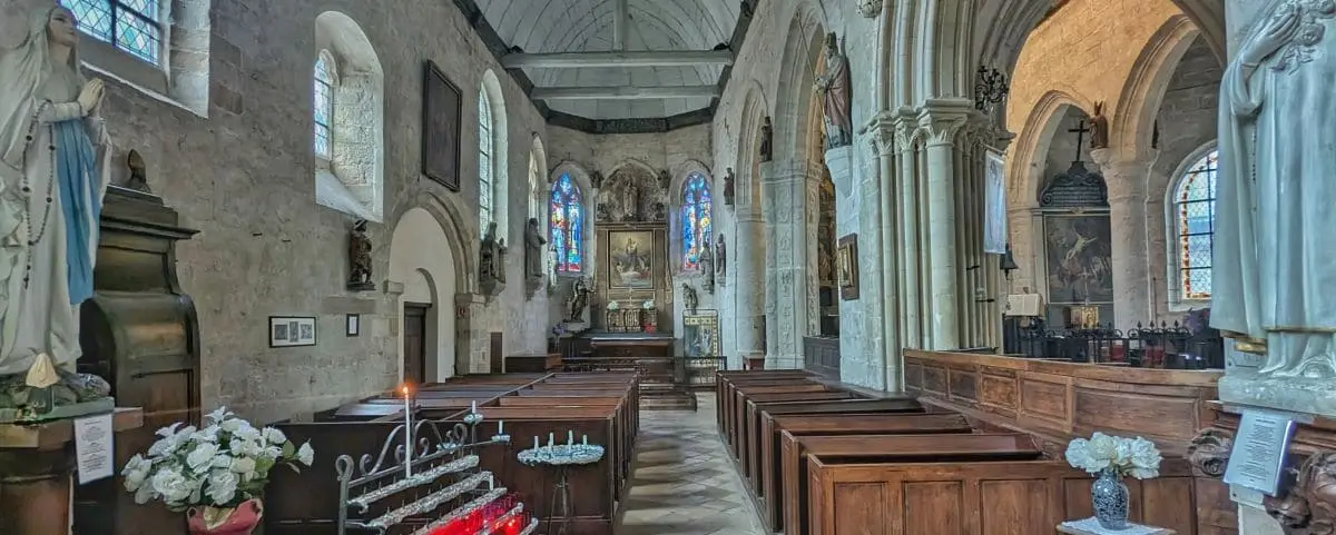 The interior of the Church of Saint Martin, featuring stone arches, stained glass windows, and wooden pews. Statues and candles adorn the space.