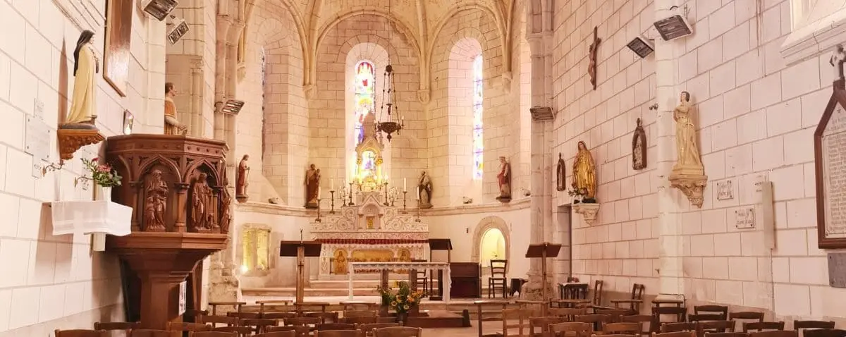 The interior of the Church of Saint-Pierre-ès-Liens in Chédigny, featuring a beautifully lit altar with statues and stained glass windows, and rows of wooden chairs.