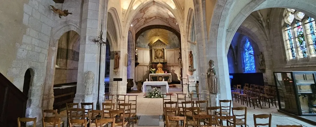 The interior of the Church of Sainte-Radegonde, showcasing its gothic architecture, arched ceilings, and rows of wooden chairs facing an altar adorned with flowers and religious statues.