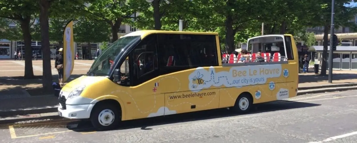 A yellow city tour bus named "Bee Le Havre" parked on a street, offering open-top seating for passengers to enjoy views of the city.