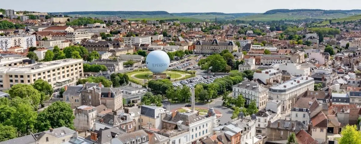 Aerial view of Epernay's city center, including the central park with a large balloon, surrounding buildings, and lush greenery.