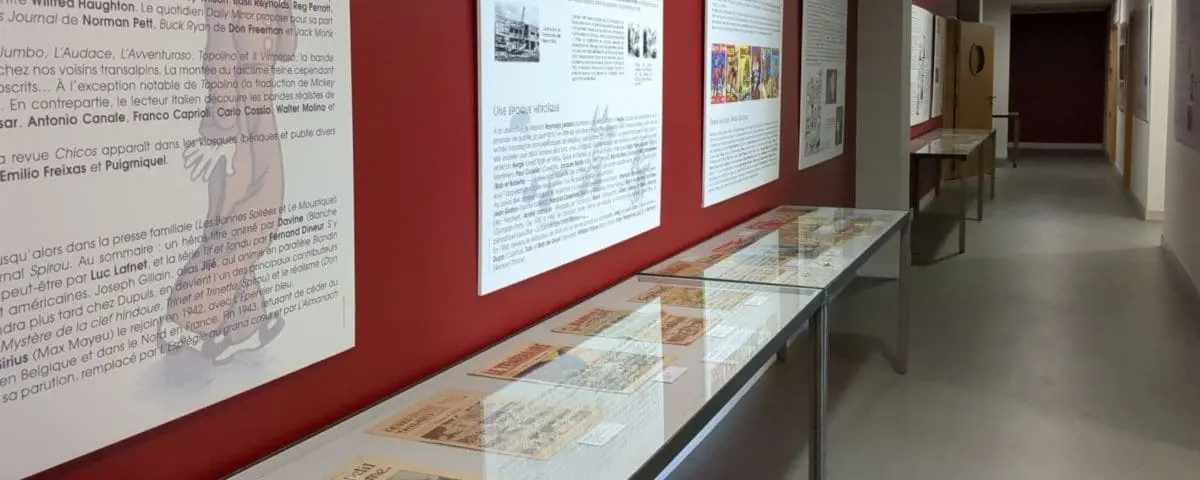 A museum exhibit with glass display cases and informational panels on the walls, showcasing various comic-related artifacts and history.