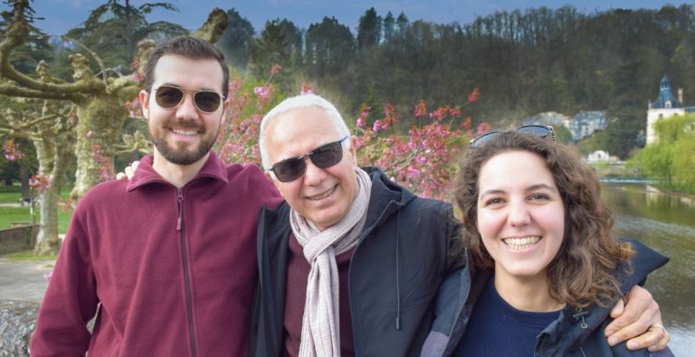 The Culture Francia team, who run a France travel guide website, pose together outdoors with blooming trees and a scenic backdrop of hills and historic buildings.