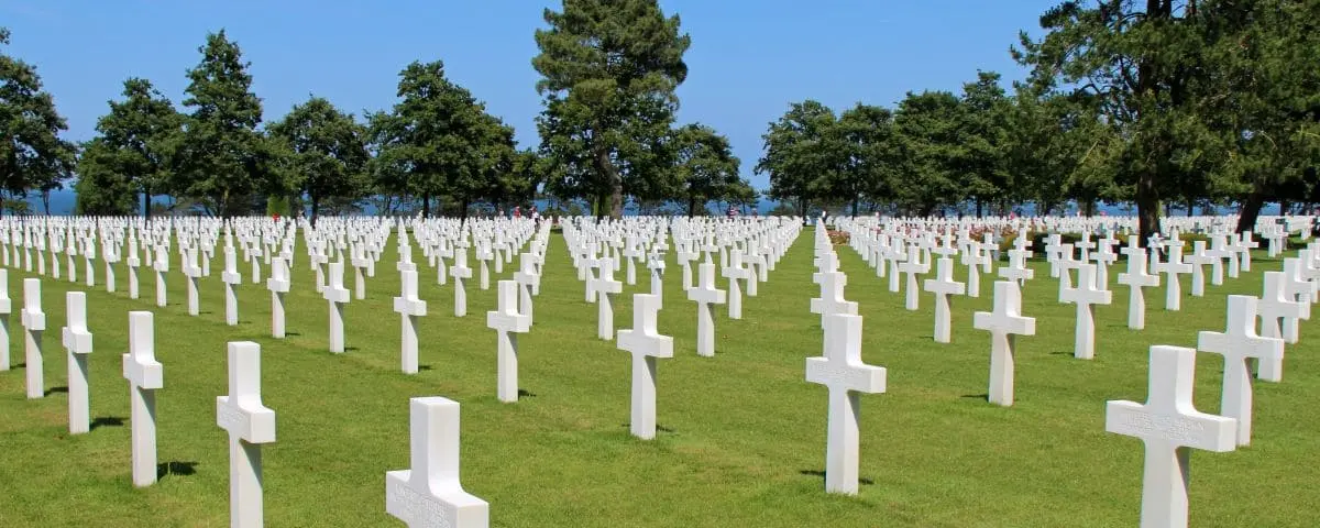 Rows of white crosses at the D-Day American Cemetery in Normandy, honoring the fallen soldiers amid green lawns and trees.