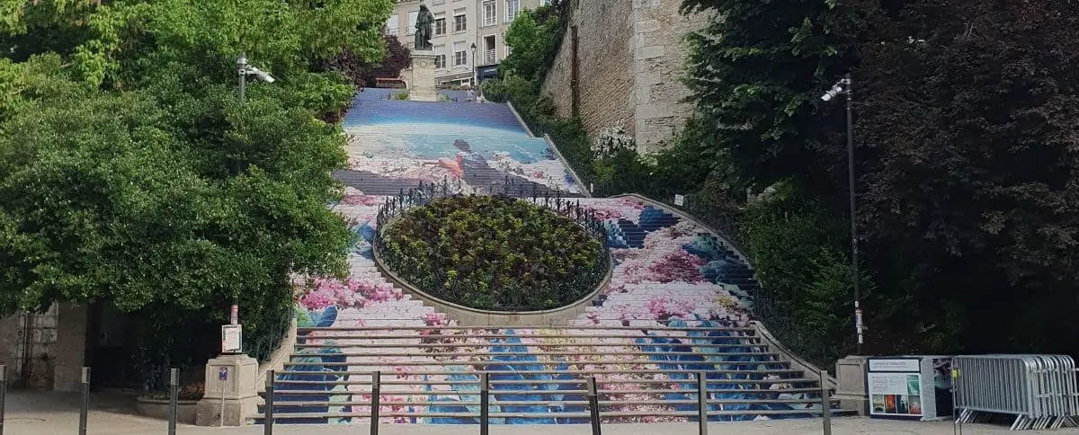 A colorful and artistic staircase adorned with a large mural, surrounded by greenery and leading up to the town.