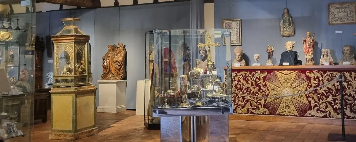 An exhibition room filled with religious artifacts, including statues, a golden cross, and other ecclesiastical items.