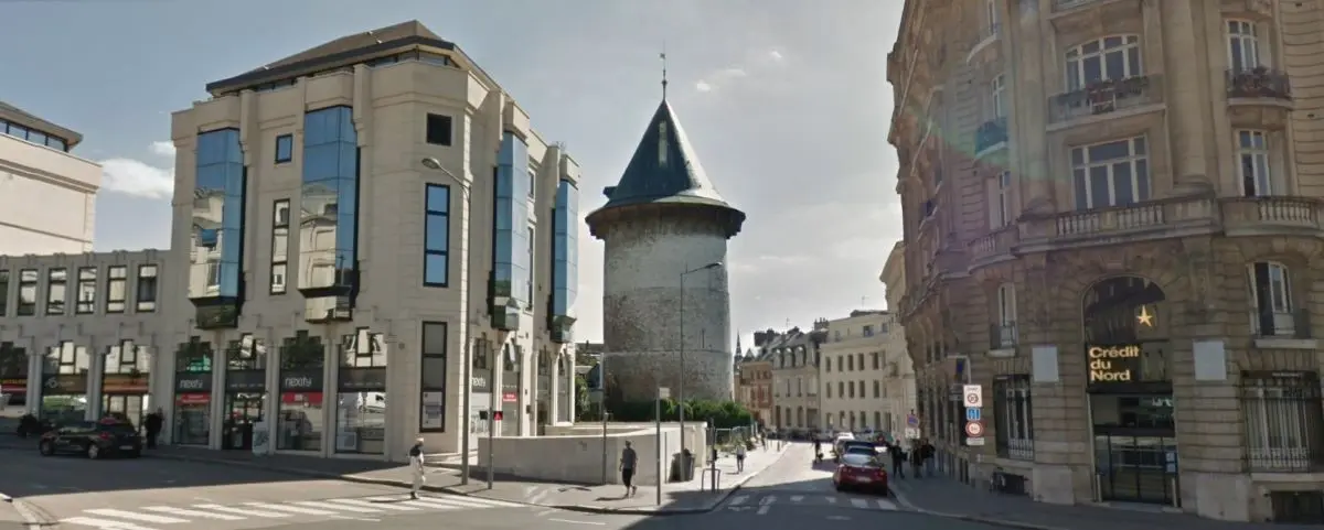 The historic Donjon of Rouen, a cylindrical stone tower set against a mix of modern and classical buildings, illustrating the blend of old and new architecture in the city.
