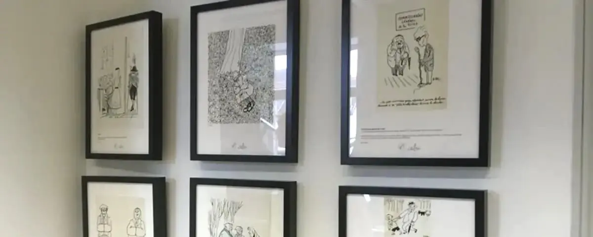 A gallery wall displaying six framed black and white cartoons and illustrations. Each frame contains a unique drawing, showcasing different scenes and characters in a minimalist style.