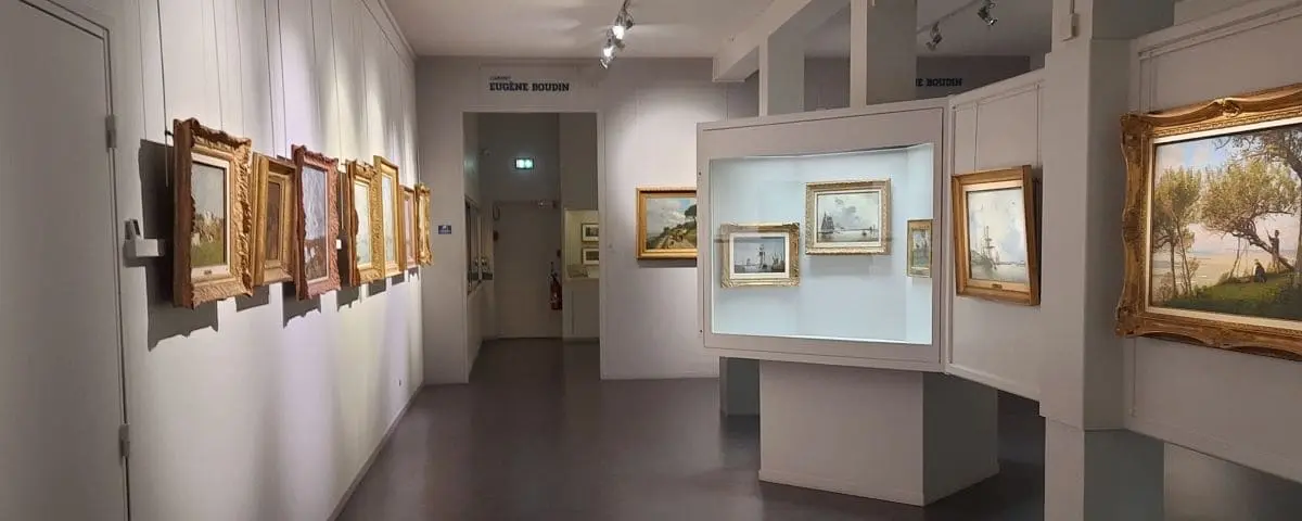 Inside the Eugene Boudin Museum, displaying a series of framed paintings on the walls. The museum features classical art pieces in a well-lit, serene setting.