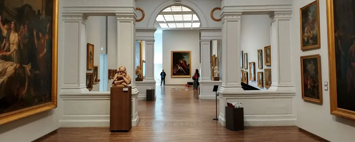 Spacious gallery hall in the Fine Arts Museum with classical paintings and sculptures, adorned with elegant architectural details.