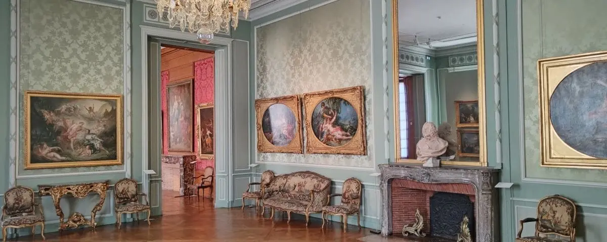 An elegantly decorated room in the Fine Arts Museum in Tours, France, featuring classical paintings, ornate furniture, and a grand chandelier.