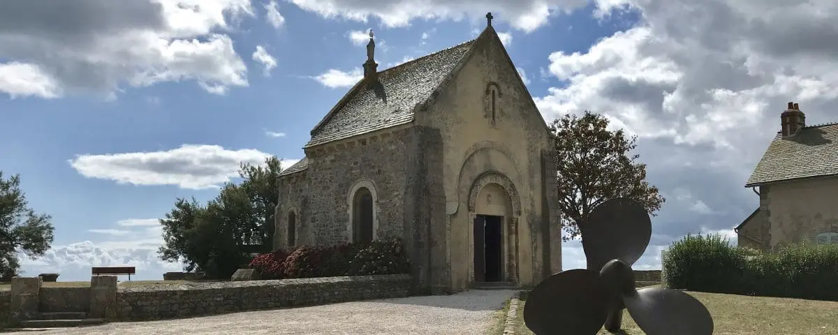 Fishermen Chapel in Saint Vaast La Hougue, a small stone chapel with a bell tower under a blue sky with scattered clouds.