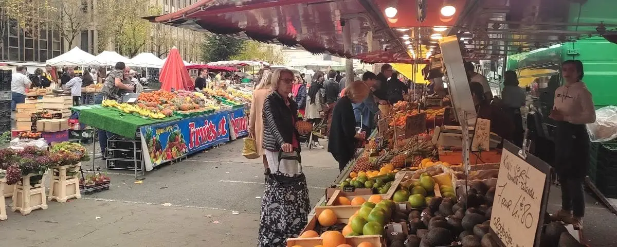 Vibrant outdoor market scene with stalls displaying a variety of fresh fruits and vegetables, and people shopping under colorful canopies.