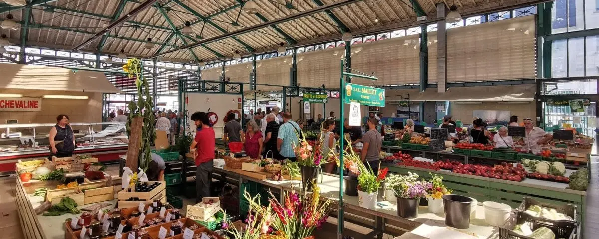 A bustling indoor market with various stalls selling fresh produce and flowers. Shoppers are seen exploring the vibrant and lively space.