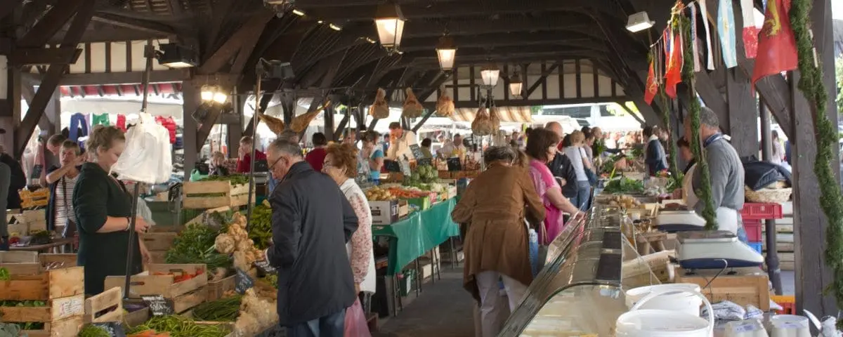 Shoppers browse stalls filled with fresh produce under the covered area of the Deauville food market.