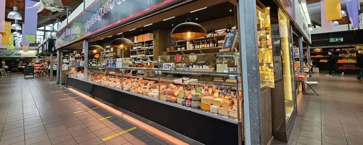 An interior shot of the food market hall in Le Havre, displaying a variety of cheeses and other products in a well-lit and neatly arranged counter.